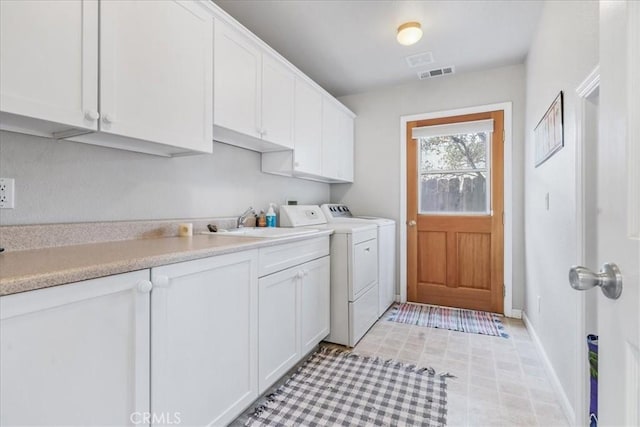 clothes washing area with separate washer and dryer, sink, and cabinets