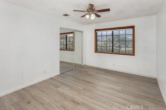 empty room featuring ceiling fan, plenty of natural light, light hardwood / wood-style floors, and a textured ceiling