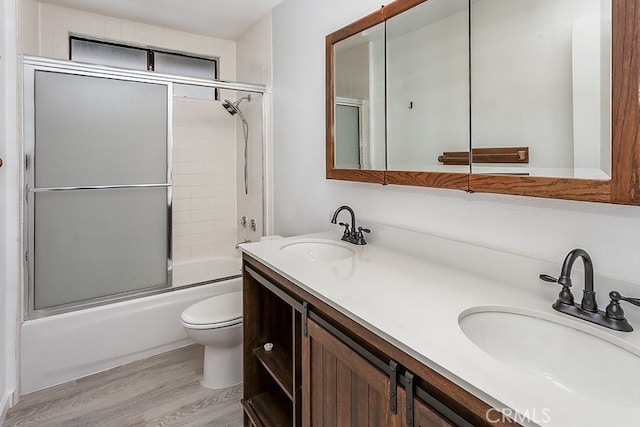 full bathroom featuring bath / shower combo with glass door, hardwood / wood-style floors, vanity, and toilet