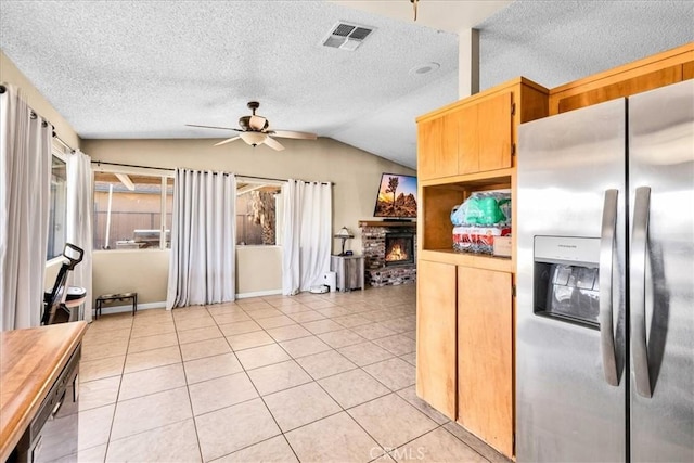 kitchen with light tile patterned flooring, lofted ceiling, ceiling fan, stainless steel refrigerator with ice dispenser, and a brick fireplace