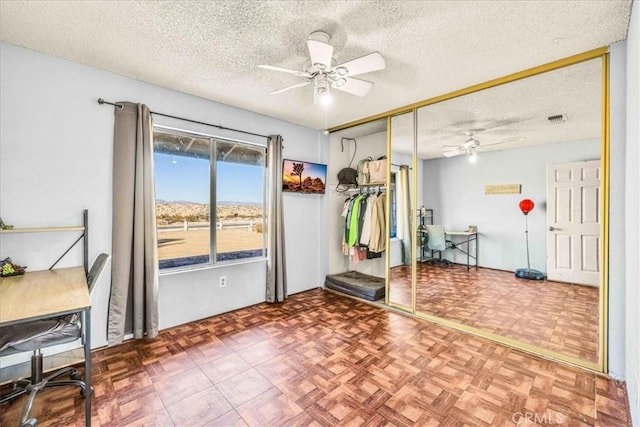 workout area with parquet floors, ceiling fan, and a textured ceiling