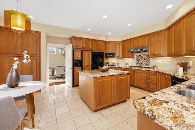 kitchen featuring decorative light fixtures, tasteful backsplash, a center island, light stone counters, and black appliances