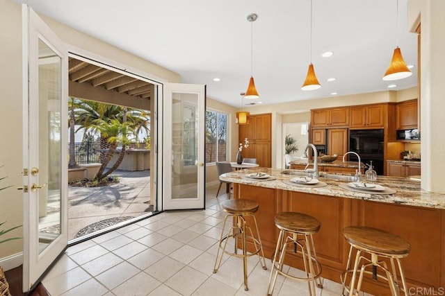 kitchen featuring light stone countertops, decorative light fixtures, black appliances, and a breakfast bar