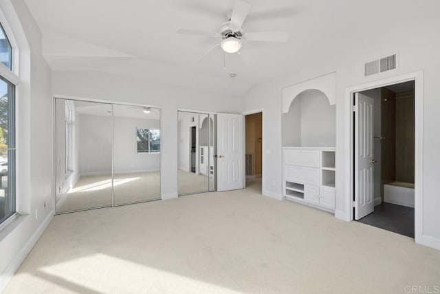 unfurnished bedroom with multiple closets, ensuite bath, ceiling fan, and light carpet