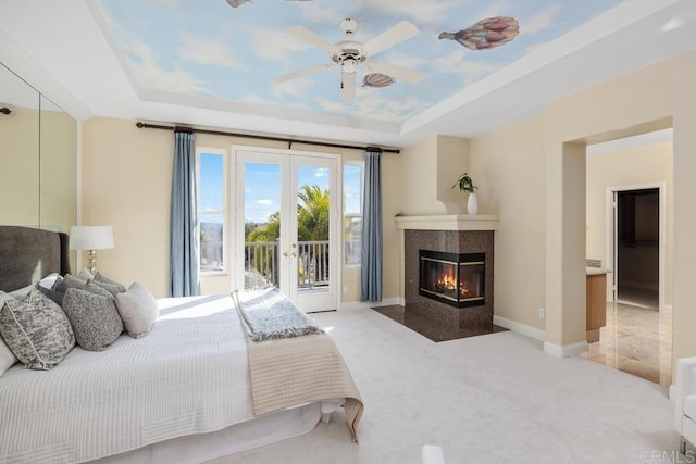 carpeted bedroom with french doors, a raised ceiling, ceiling fan, access to exterior, and a tiled fireplace