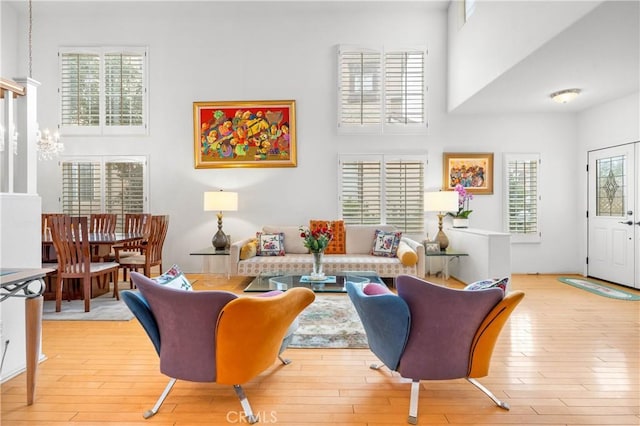 living room featuring an inviting chandelier, a towering ceiling, and light wood-type flooring