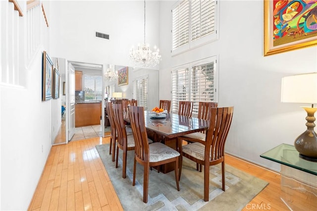 dining space with a towering ceiling, light hardwood / wood-style flooring, and a chandelier