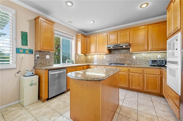 kitchen with light stone countertops, a kitchen island, stainless steel appliances, under cabinet range hood, and crown molding