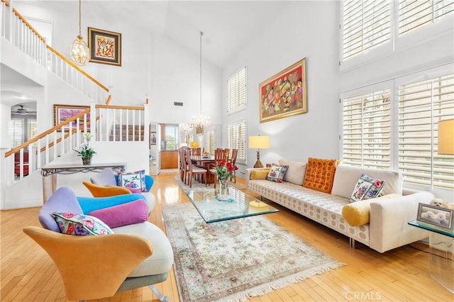 living room featuring a towering ceiling, wood-type flooring, a chandelier, and stairs