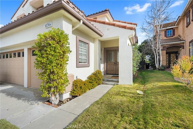 view of exterior entry featuring a yard, an attached garage, stucco siding, concrete driveway, and a tiled roof