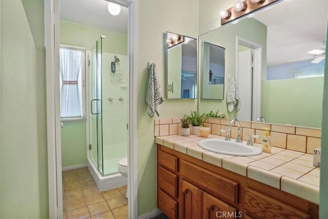 bathroom with a shower with door, ceiling fan, tile patterned flooring, vanity, and toilet