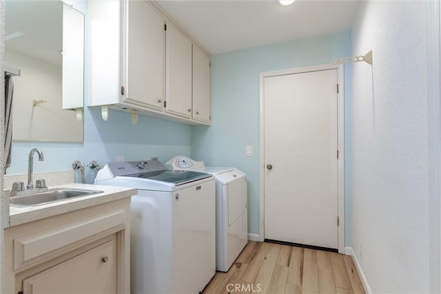 clothes washing area with a sink, baseboards, light wood-type flooring, cabinet space, and washing machine and clothes dryer