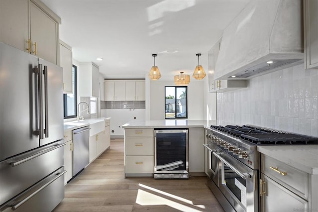 kitchen with sink, premium appliances, custom range hood, pendant lighting, and beverage cooler