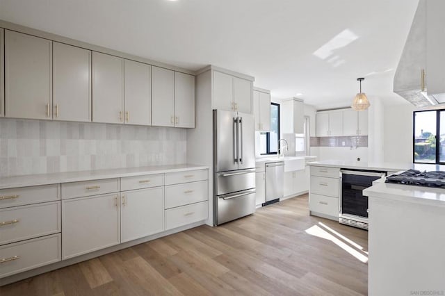 kitchen with appliances with stainless steel finishes, pendant lighting, beverage cooler, backsplash, and light wood-type flooring