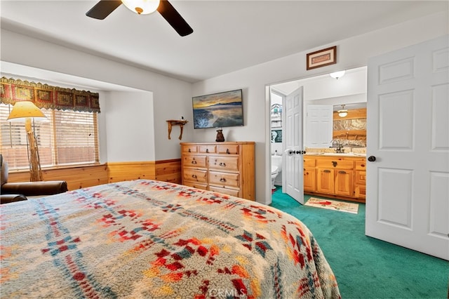 bedroom with sink, ensuite bath, ceiling fan, dark colored carpet, and wood walls