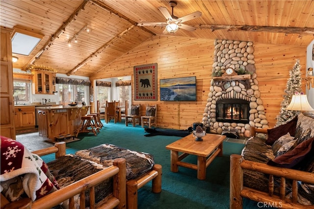 living room with wood ceiling, rail lighting, carpet flooring, a stone fireplace, and vaulted ceiling