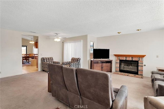 living room with ceiling fan, a brick fireplace, light carpet, and a textured ceiling