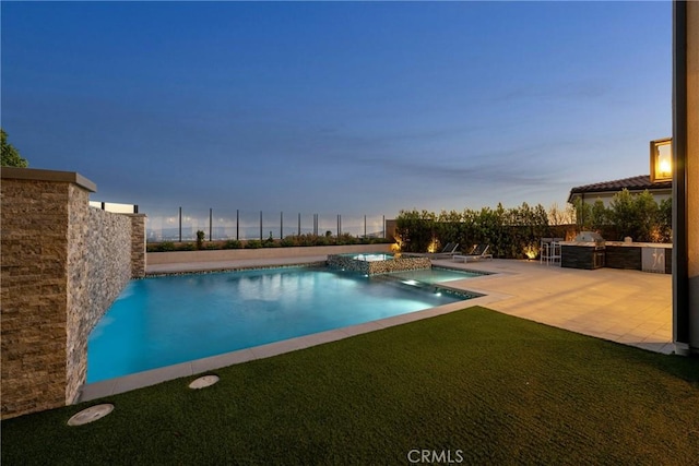 pool at dusk featuring a lawn, a patio, pool water feature, and exterior kitchen