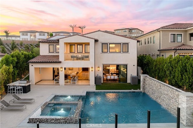 back house at dusk with a swimming pool with hot tub, cooling unit, a patio, pool water feature, and a balcony