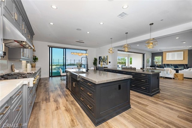 kitchen with a kitchen island with sink, pendant lighting, light hardwood / wood-style flooring, and light stone countertops