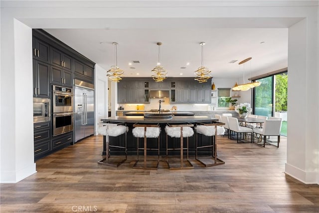 20436 W Liverpool Way, Porter Ranch, CA 91326 - kitchen with built in appliances, a kitchen breakfast bar, baseboards, a center island with sink, and dark wood finished floors