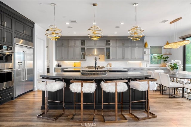 kitchen with a large island, wall chimney range hood, pendant lighting, a breakfast bar, and stainless steel appliances