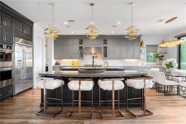 20436 W Liverpool Way, Porter Ranch, CA 91326 - kitchen featuring stainless steel appliances, extractor fan, wood finished floors, glass insert cabinets, and a breakfast bar