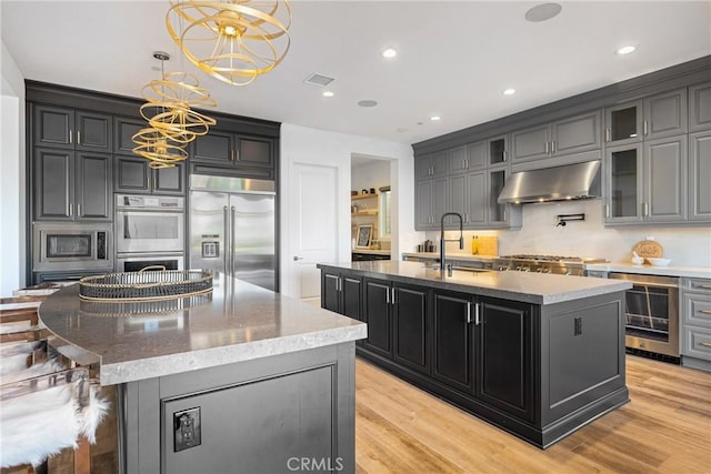 kitchen featuring built in appliances, a kitchen island with sink, hanging light fixtures, and exhaust hood