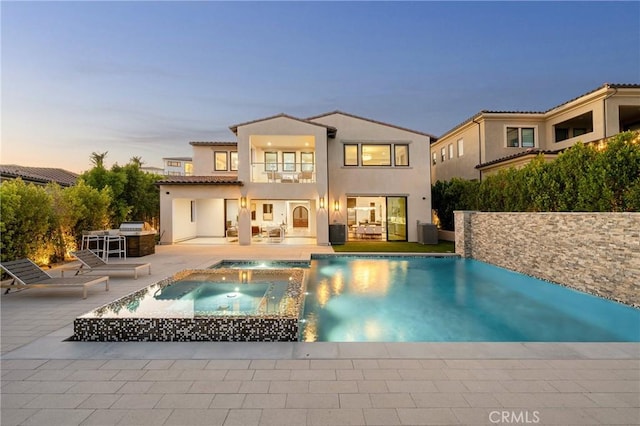 20436 W Liverpool Way, Porter Ranch, CA 91326 - back of property at dusk featuring a balcony, a patio area, central AC, stucco siding, and a pool with connected hot tub
