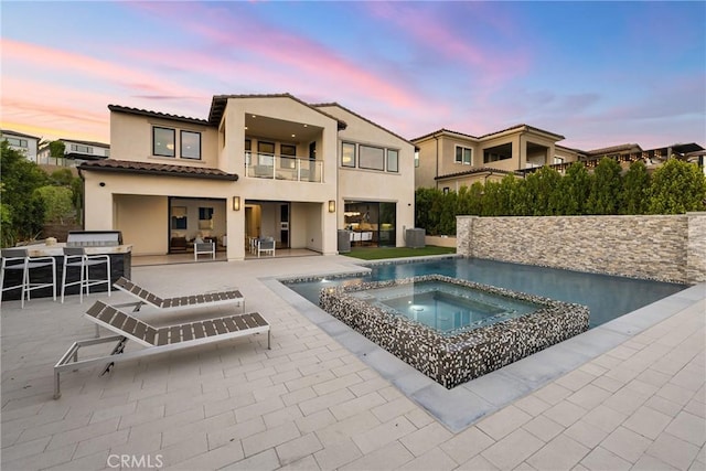 pool at dusk featuring an in ground hot tub, an outdoor bar, and a patio