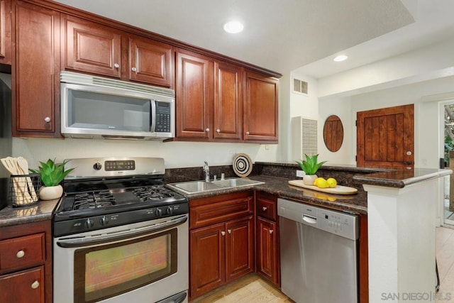 kitchen with stainless steel appliances, kitchen peninsula, sink, and dark stone countertops