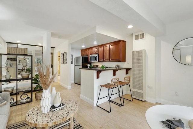 kitchen with stainless steel appliances, a breakfast bar, light hardwood / wood-style flooring, and kitchen peninsula