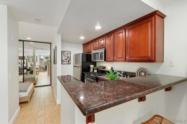 kitchen with appliances with stainless steel finishes, a breakfast bar, dark stone countertops, kitchen peninsula, and light hardwood / wood-style flooring