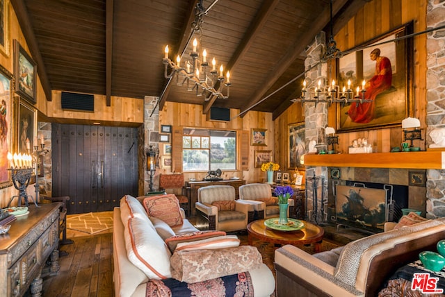 living room with dark wood-type flooring, wooden walls, a stone fireplace, and a chandelier