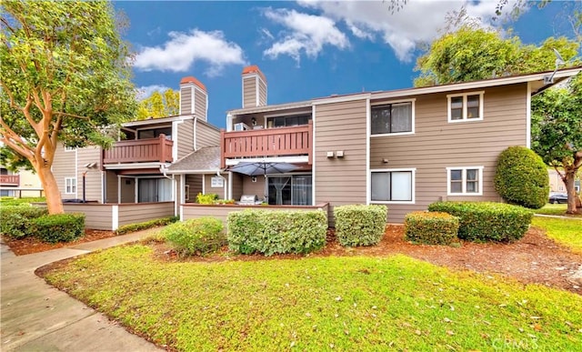 rear view of property with a balcony, a lawn, and a chimney