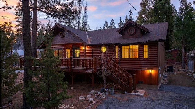 view of front of home featuring a shingled roof, central AC unit, log veneer siding, stairs, and a deck