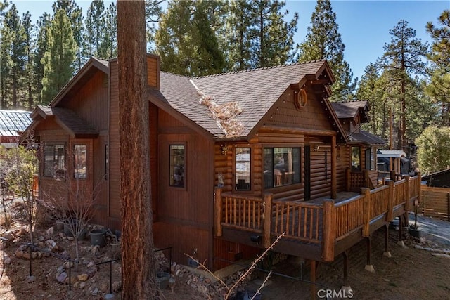 rear view of property featuring roof with shingles, a chimney, and a wooden deck