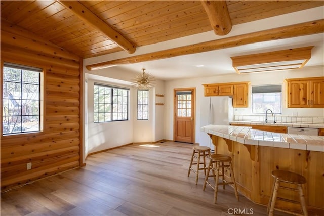 kitchen with beamed ceiling, a sink, tile countertops, and a breakfast bar area