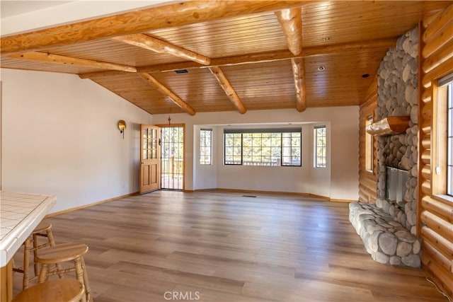 unfurnished living room with vaulted ceiling with beams, wood ceiling, wood finished floors, and a stone fireplace