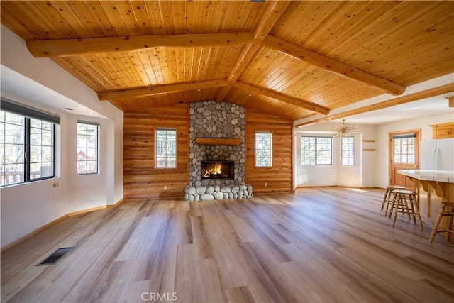 unfurnished living room with visible vents, light wood-style flooring, vaulted ceiling with beams, log walls, and a fireplace