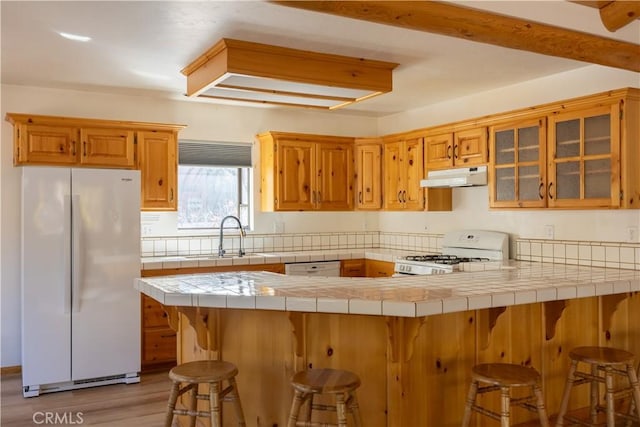 kitchen with under cabinet range hood, a peninsula, white appliances, a sink, and glass insert cabinets