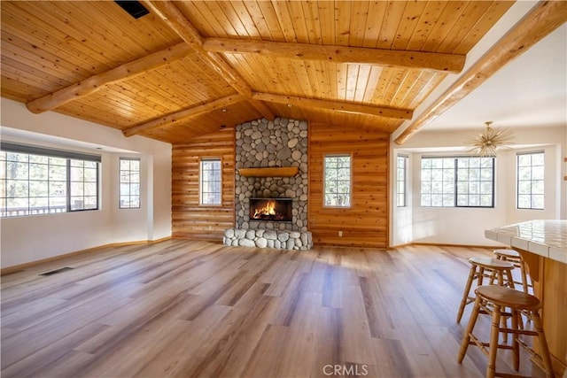 unfurnished living room featuring vaulted ceiling with beams, plenty of natural light, wood finished floors, and a stone fireplace