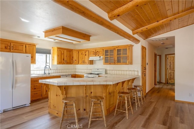 kitchen with under cabinet range hood, white appliances, a breakfast bar, a sink, and tile counters