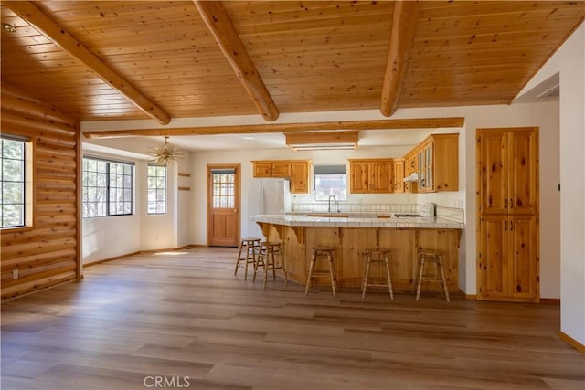 kitchen featuring a breakfast bar, light wood finished floors, tile counters, freestanding refrigerator, and a peninsula