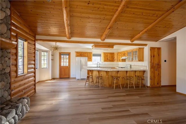 kitchen with glass insert cabinets, freestanding refrigerator, a peninsula, under cabinet range hood, and a kitchen bar