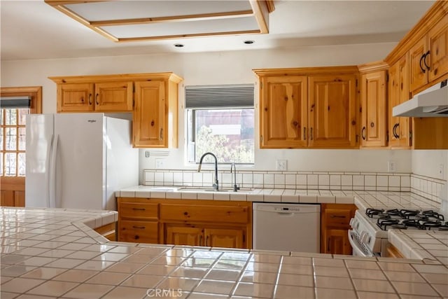 kitchen with white appliances, a sink, tile countertops, and under cabinet range hood