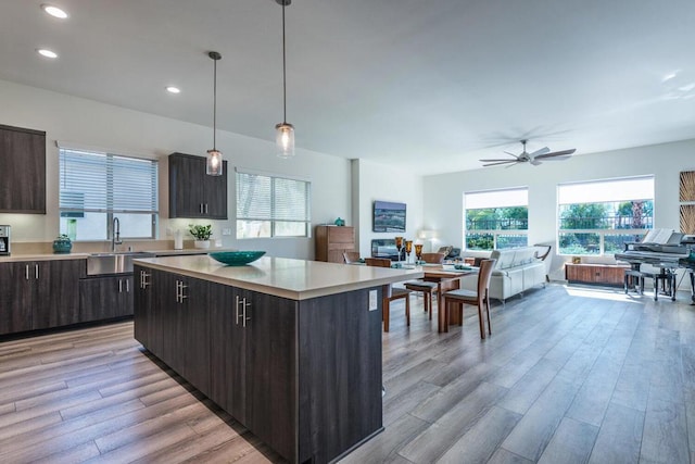 kitchen with sink, light hardwood / wood-style flooring, dark brown cabinets, a center island, and decorative light fixtures