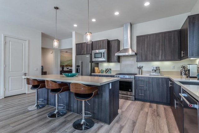 kitchen with dark brown cabinets, high end appliances, a kitchen island, decorative light fixtures, and wall chimney exhaust hood