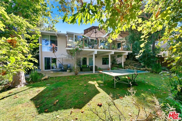 back of property with a balcony, a patio area, and a lawn