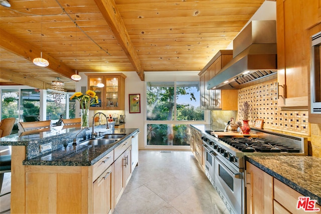 kitchen featuring sink, tasteful backsplash, dark stone counters, stainless steel appliances, and wall chimney range hood